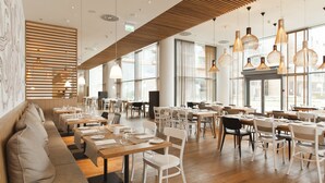 Un restaurante espacioso con varias mesas y sillas para comer, pisos de madera y amplias ventanas que dejan entrar luz natural.