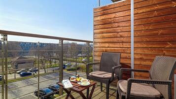 Ein Balkon mit Korbstühlen, einem Tisch mit einer Speiseplatte und einer Tasse, und Blick auf einen Parkplatz und Gebäude.