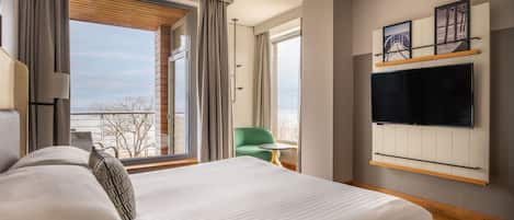A modern hotel room with a large bed, a TV mounted on the wall, and a view of the city through the window.