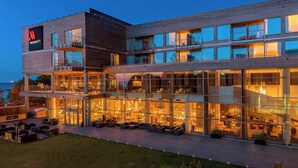 Un hotel de varios pisos con un diseño moderno, que cuenta con un área de bar/lounge en la planta baja, mesas al aire libre y balcones en cada piso.