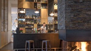 Una zona de bar con mostrador de madera, taburetes y una pared de piedra con chimenea.