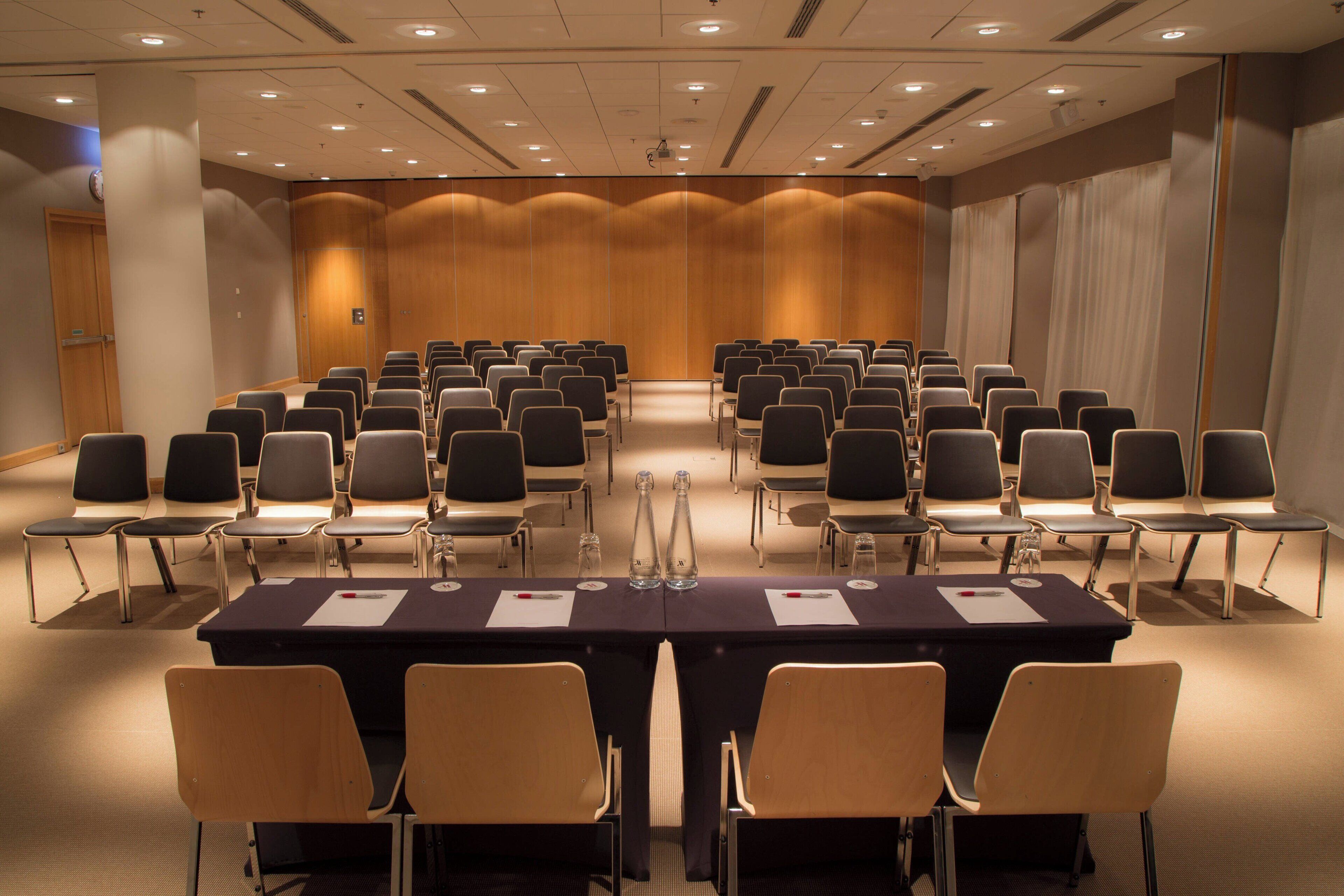 Un salón de conferencias con filas de sillas, una mesa larga y un atril.