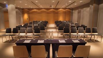 Un salón de conferencias con filas de sillas, una mesa larga y un atril.