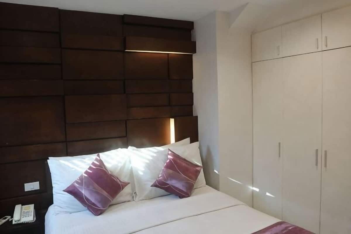 Una cama con ropa de cama blanca y dos almohadas, un cabecero de madera y un armario de dos puertas.