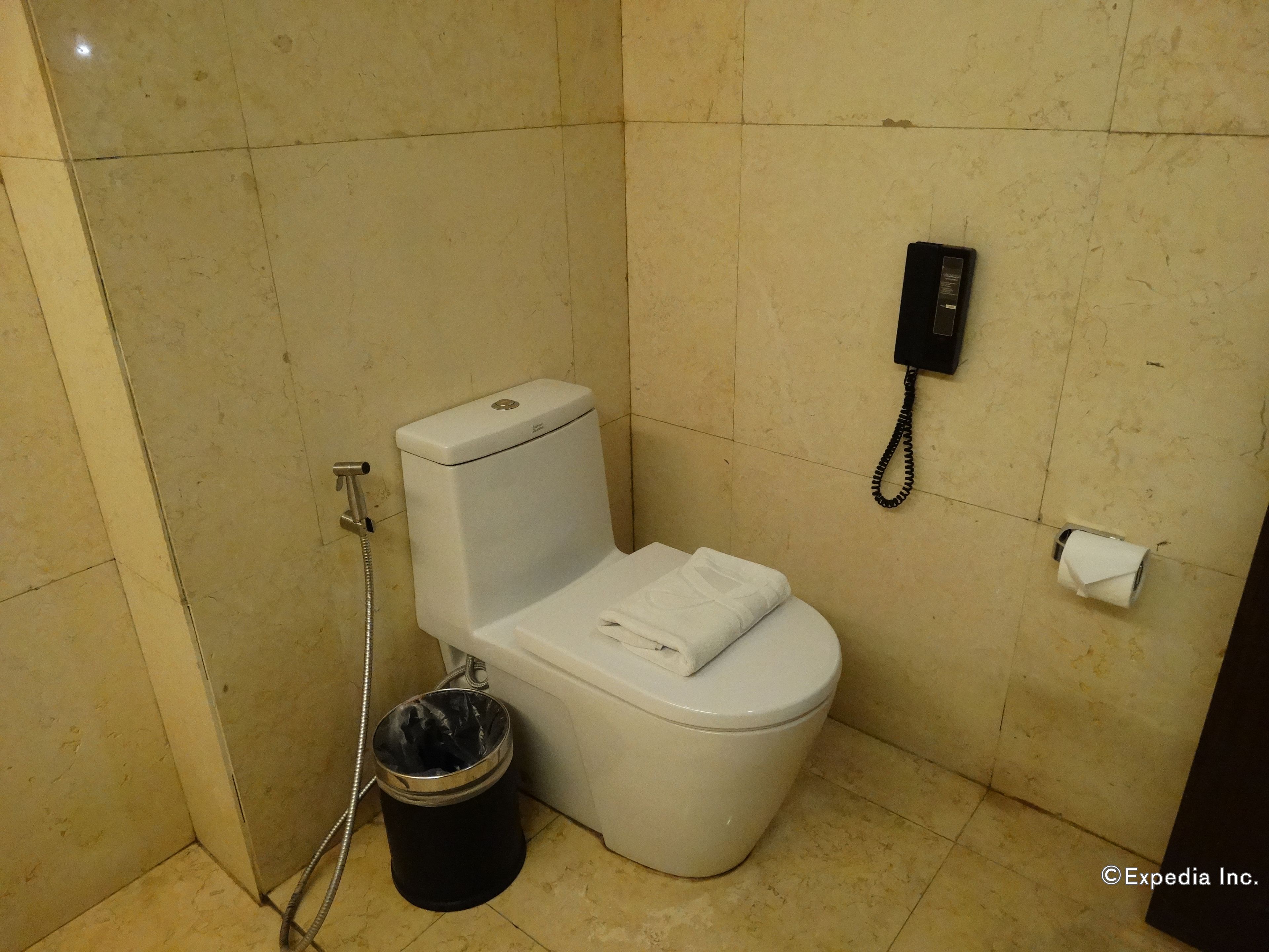 A small, tiled bathroom with a toilet, a trash bin, and a telephone.