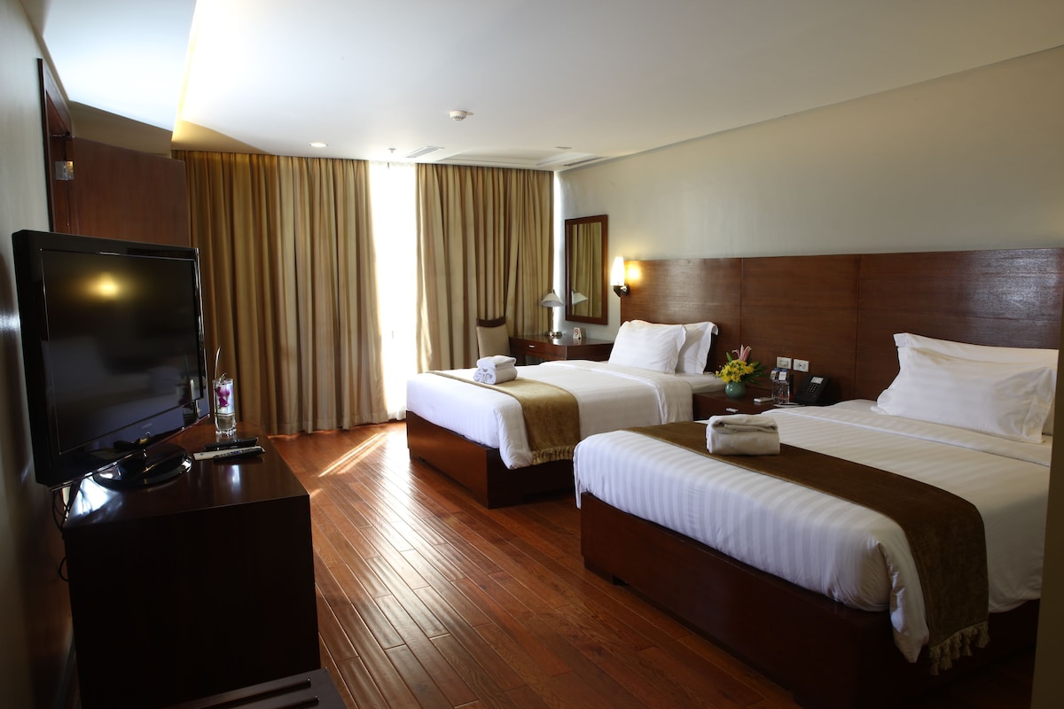 Quarto de hotel com duas camas, televisão, escrivaninha e espelho.