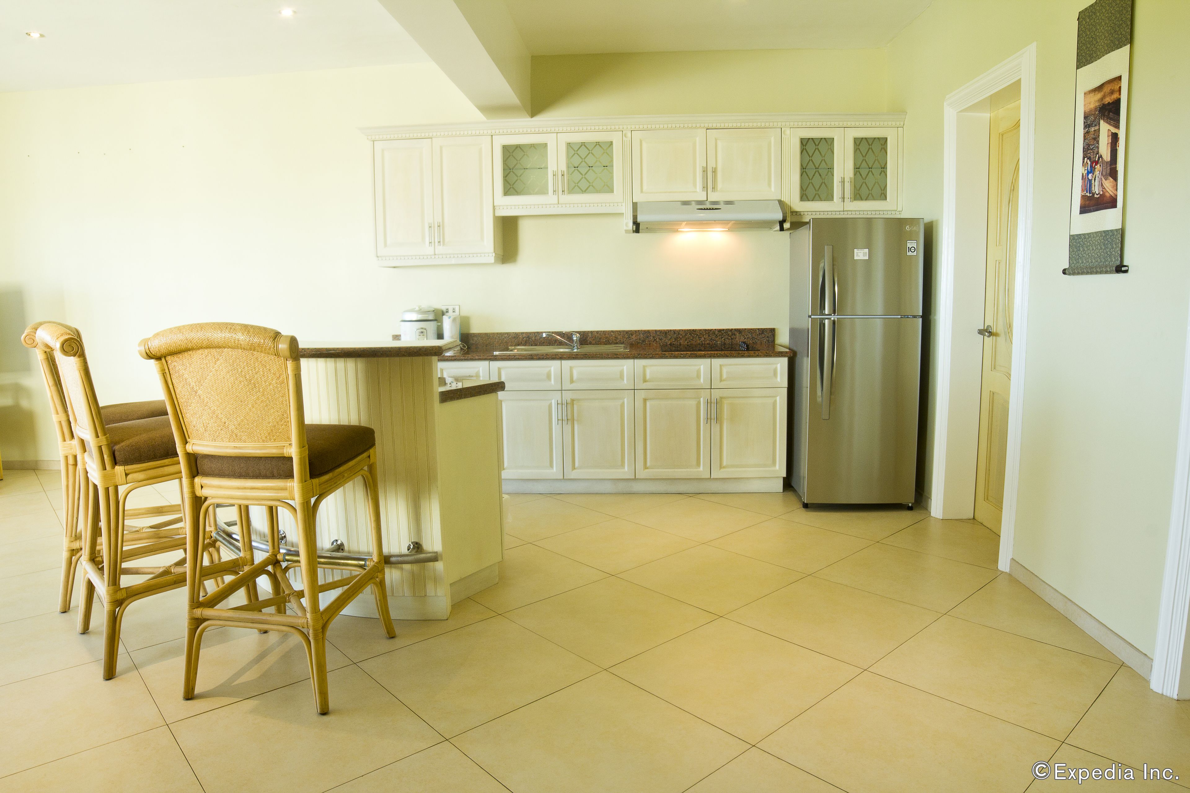 Una cocina con armarios blancos, un refrigerador de acero inoxidable y un comedor con sillas de mimbre.