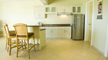 Una cocina con armarios blancos, un refrigerador de acero inoxidable y un comedor con sillas de mimbre.