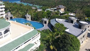 A resort with a large swimming pool, multiple buildings with stone towers, and a view of the ocean. - Lingganay Boracay Hotel Resort (Boracay Island)
