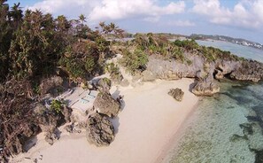 A beach with clear turquoise water, rocky outcrops, and dense tropical vegetation.