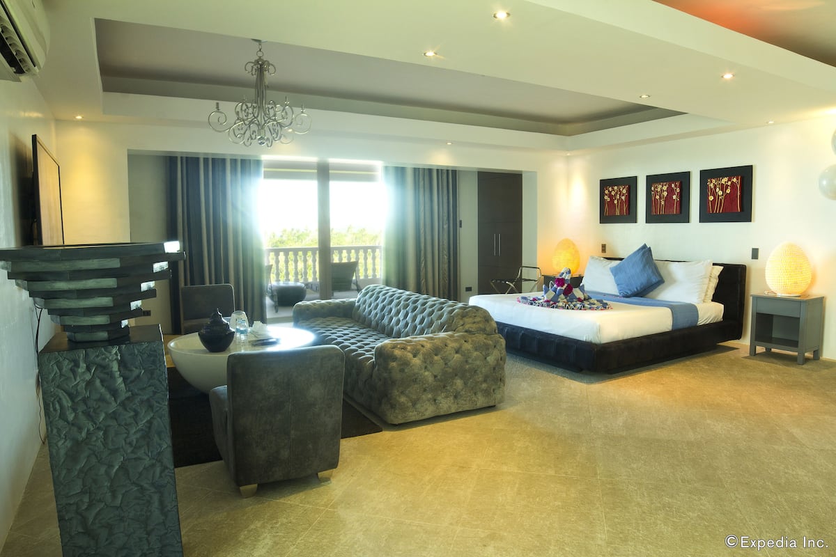 Una habitación de hotel moderna con cama, sofá, mesa de comedor y balcón.
