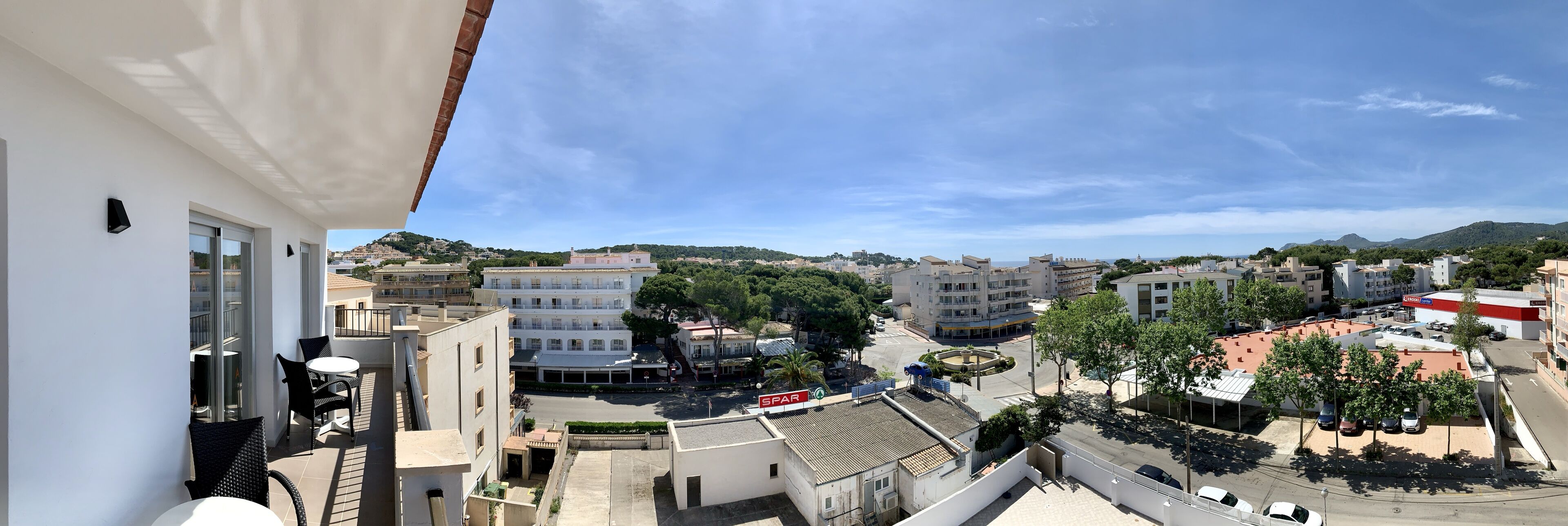 Vista desde un balcón con vista a un paisaje urbano que incluye edificios, una glorieta y una colina al fondo.