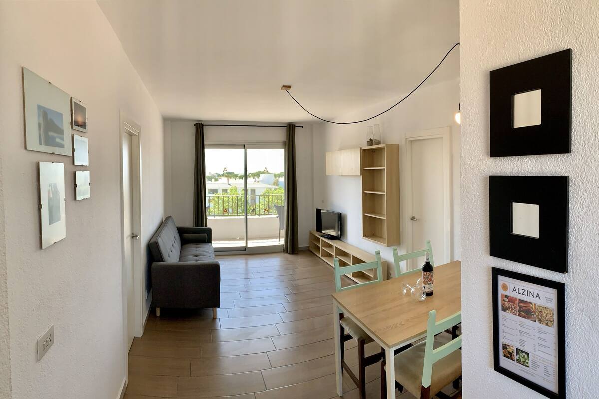 Una sala de estar moderna con un sofá, televisión y comedor con mesa y sillas.
