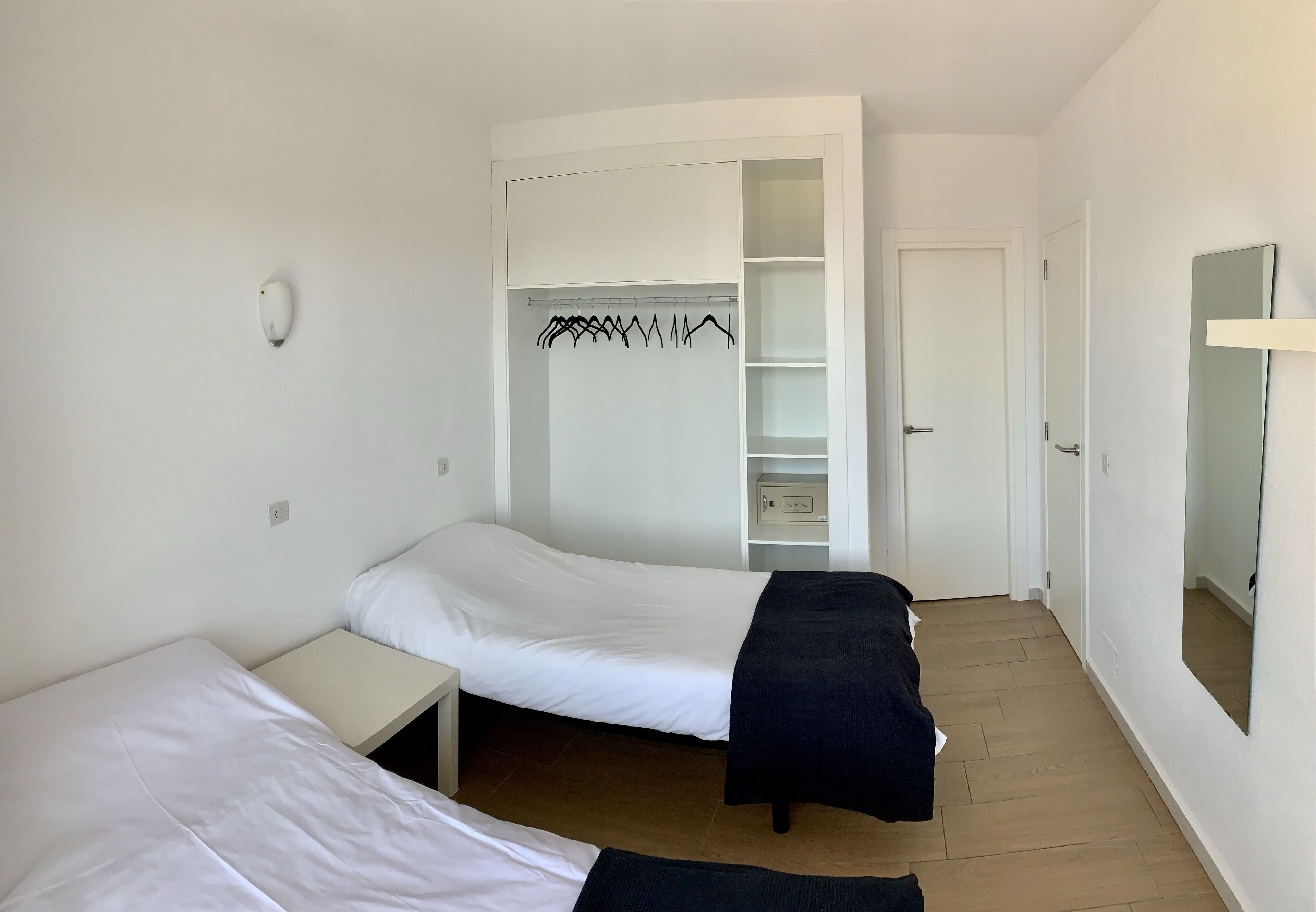 A small, clean room with two beds, a white wardrobe, and a mirror.