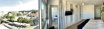 Habitación de hotel con un ventanal grande que ofrece vistas de la ciudad, una cama, un televisor y un vestidor.