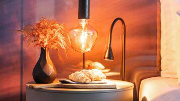 A bedside table with a lamp, a vase with dried flowers, and a plate with croissants.