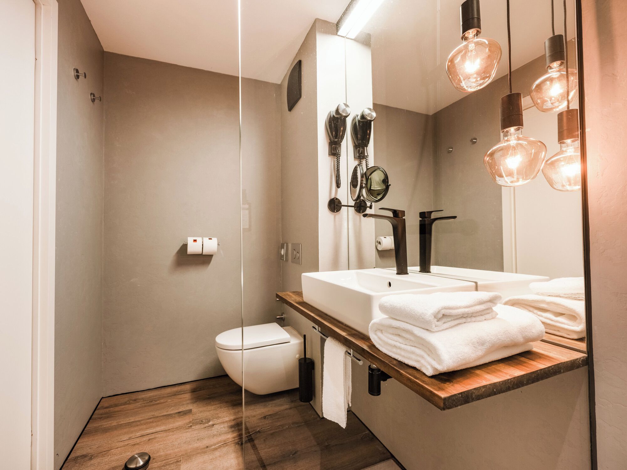 Un baño moderno con tocador de madera, inodoro y un espejo grande.