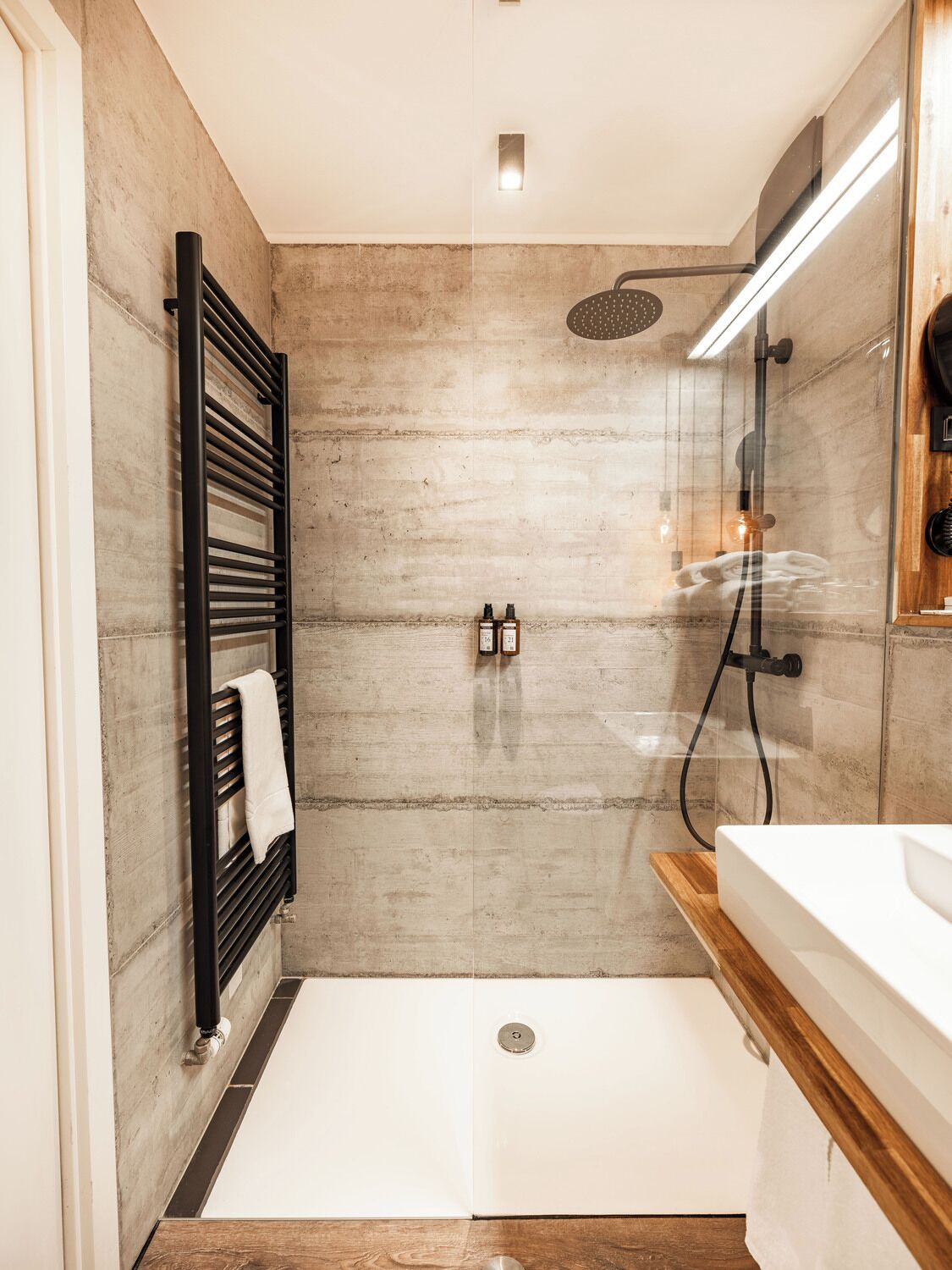 Un bagno moderno con doccia vetro, portasciugamani nero e mobile lavabo in legno.