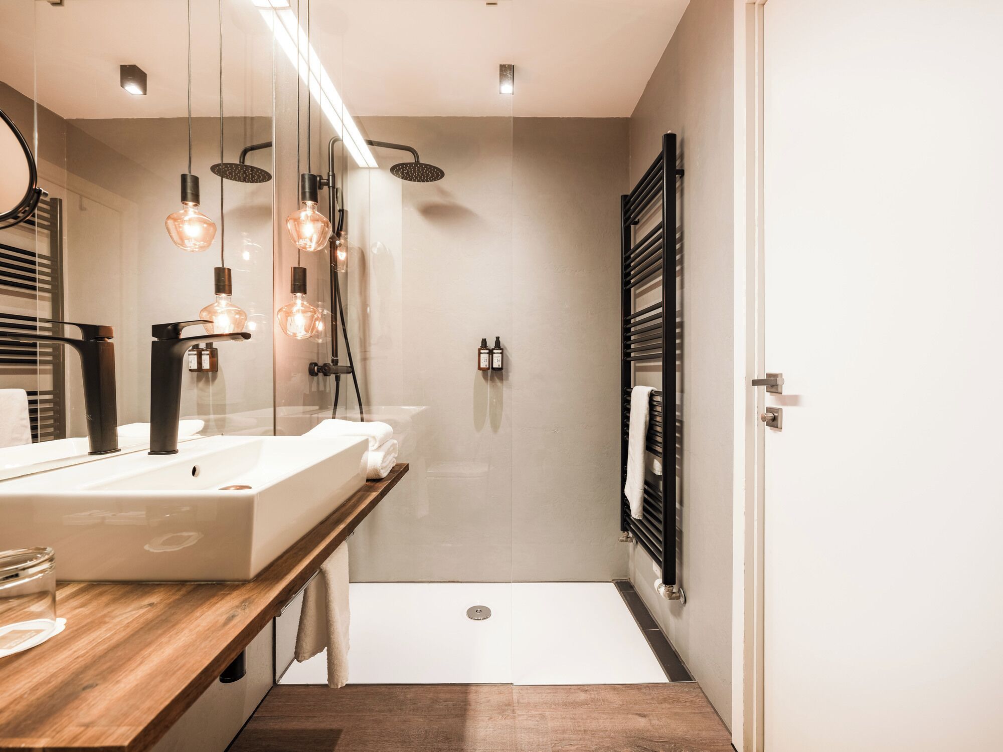 A modern bathroom with a wooden vanity, a glass shower enclosure, and a black towel rack.