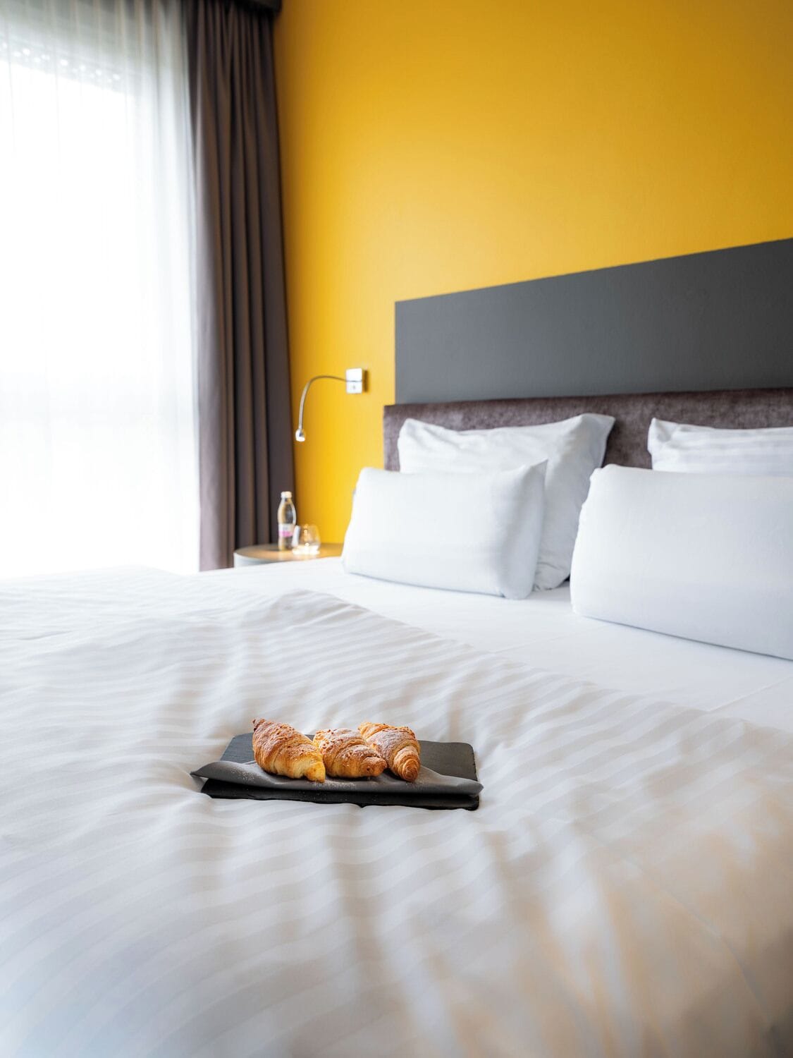 Une chambre d’hôtel avec un lit, une table de chevet, une lampe et une fenêtre avec des rideaux.