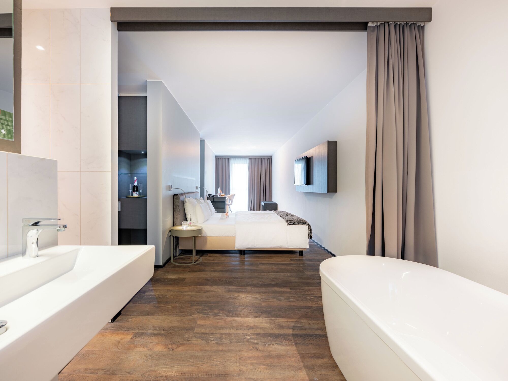 Een moderne hotelkamer met een groot bed, een aparte badkamer met bad, een bureau en een aan de muur bevestigde televisie.
