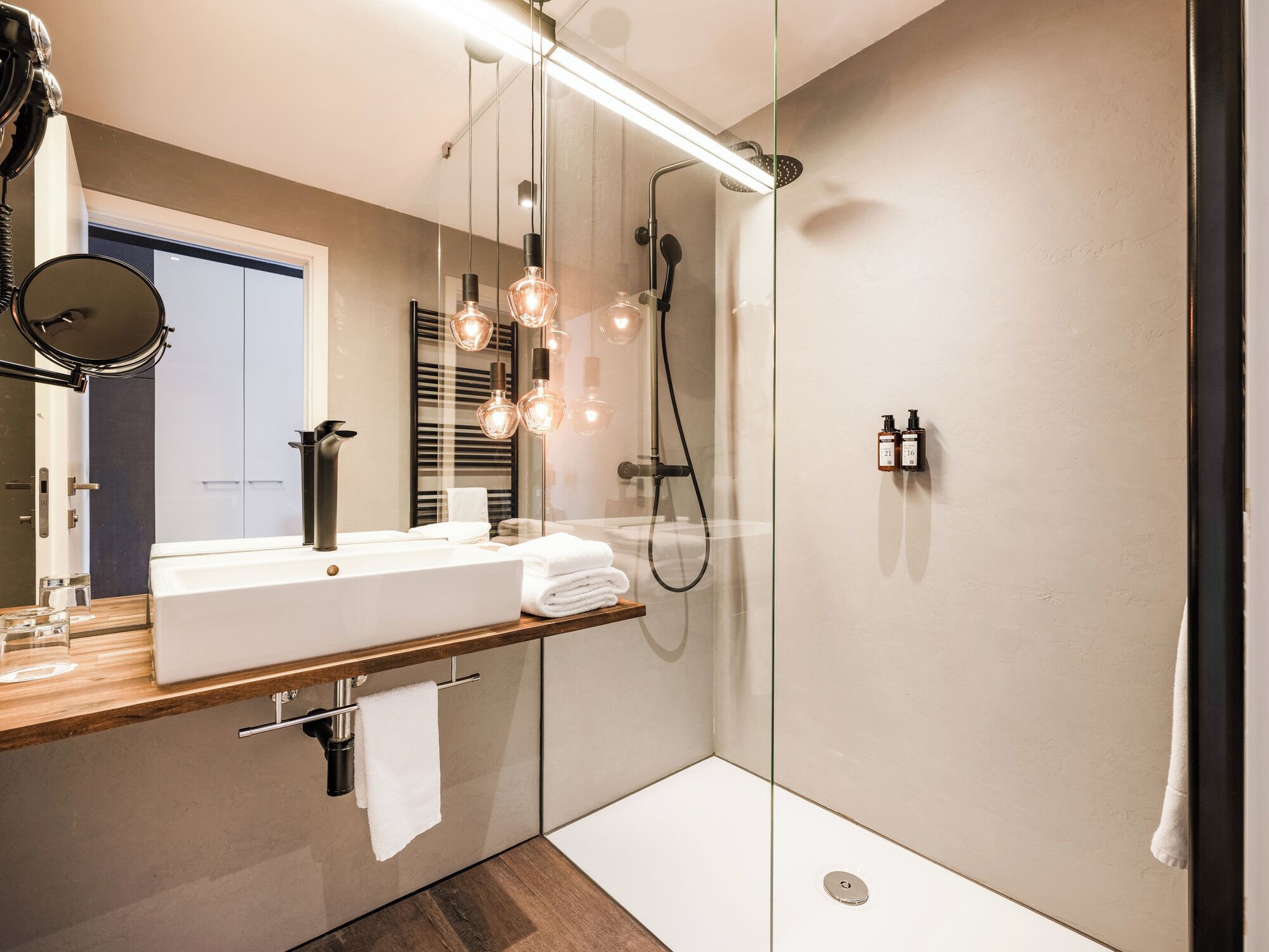 Un baño moderno con ducha de vidrio, un espejo grande e iluminación colgante.