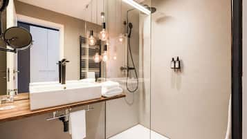 Un baño moderno con ducha de vidrio, un espejo grande e iluminación colgante.