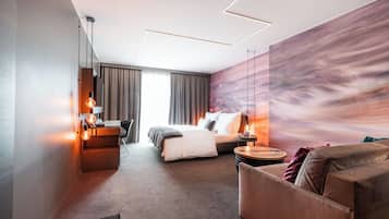 Ett modernt hotellrum med en säng, ett skrivbord, en stol, en soffa och en stor väggmålning.