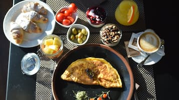 A table with a variety of breakfast items including croissants, tomatoes, olives, a fruit bowl, a bowl of yogurt with berries, granola, a glass of orange juice, and a cup of coffee.
