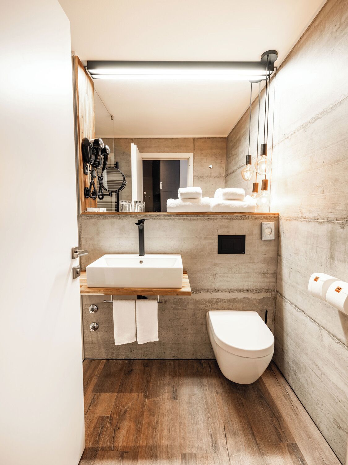 Ein modernes Badezimmer mit einem Holzkosmetikschrank, einem weißen Waschbecken, einer Toilette und einem Spiegel.