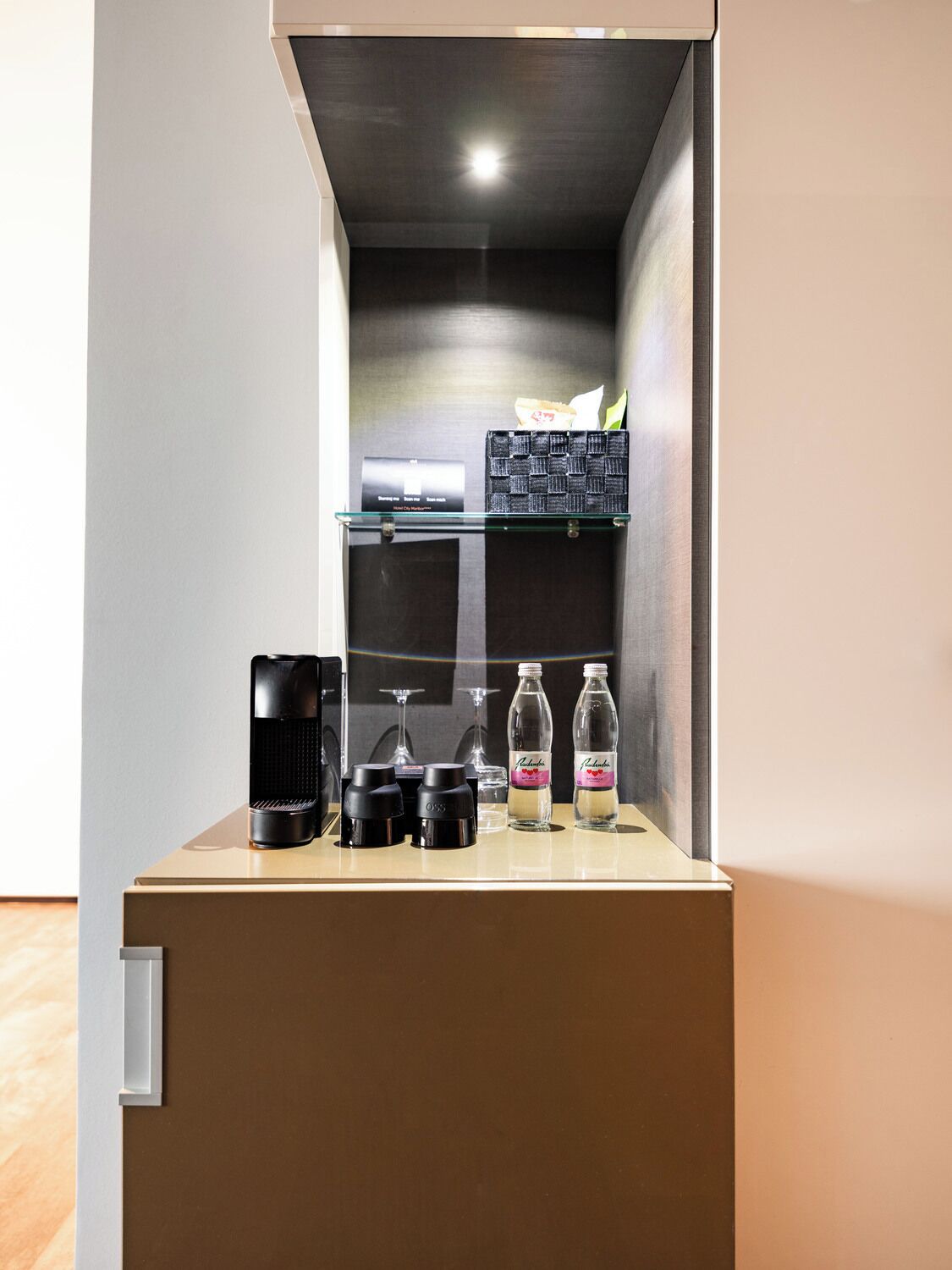 A compact kitchenette with a coffee maker, two condiment bottles, and a glass shelf with condiments.