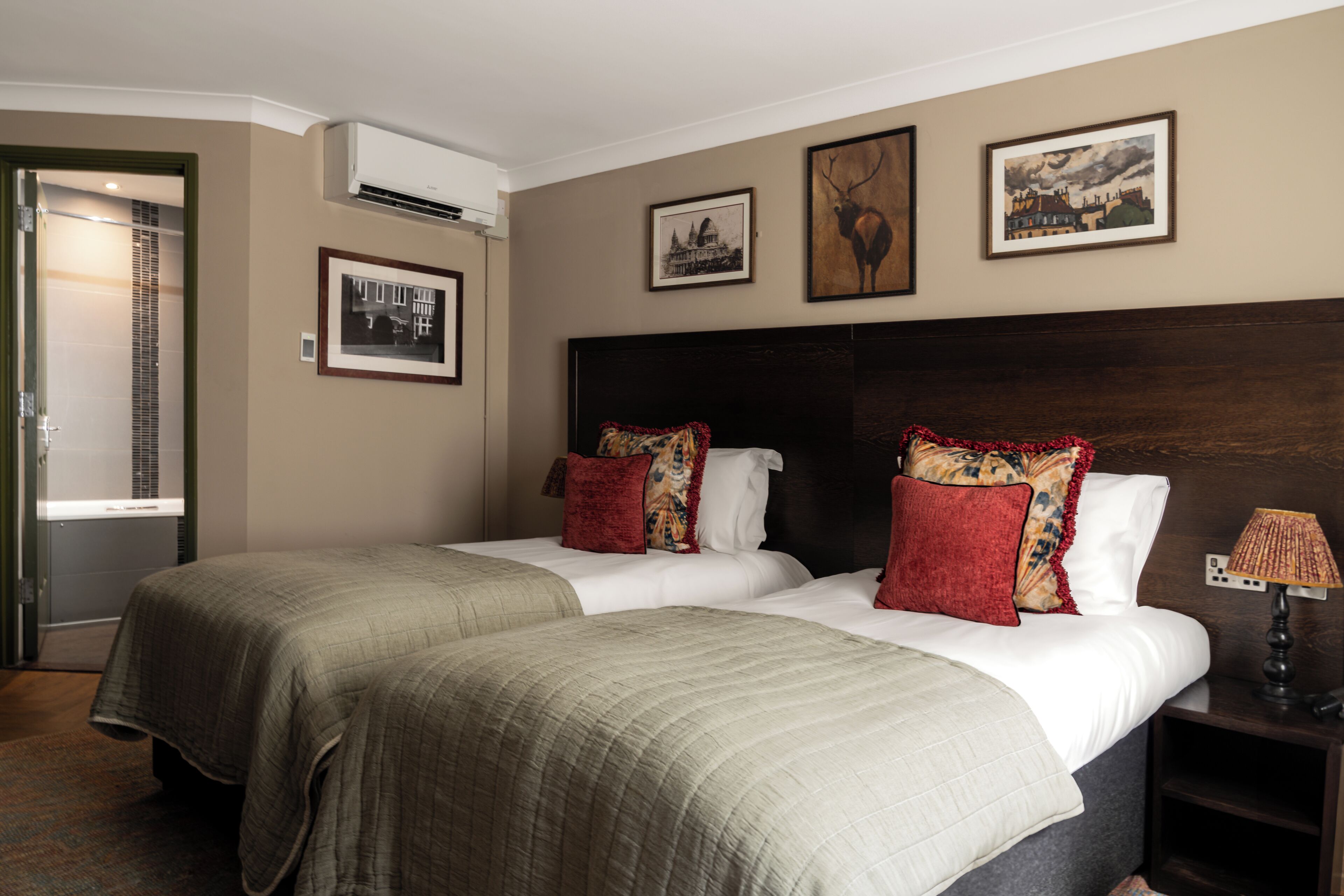 A hotel room with two beds, a nightstand with a lamp, and three framed pictures on the wall.