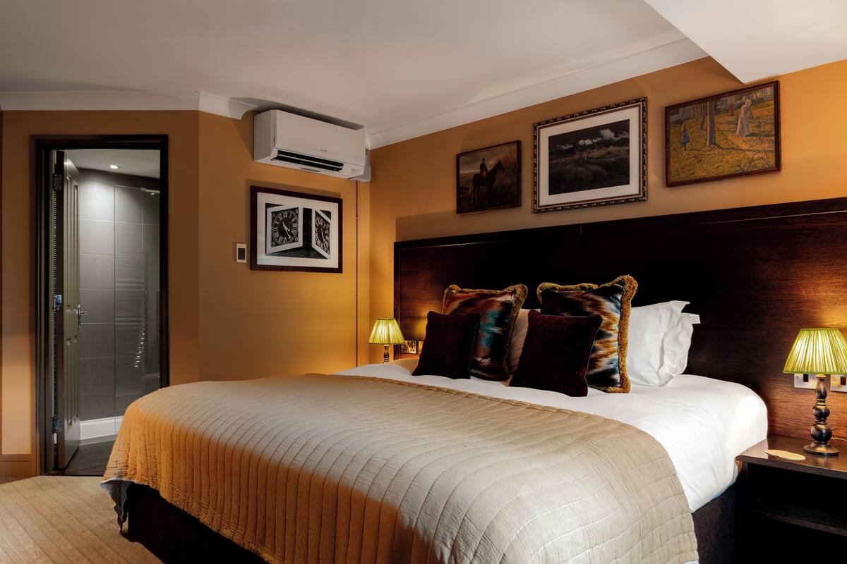 A hotel room with a large bed, a wooden headboard, a nightstand with a lamp, and framed artwork on the wall.