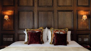 A hotel room with a large bed, two decorative pillows, wooden paneling on the walls, and wall-mounted lamps. - The Rose & Crown Wimbledon (London)