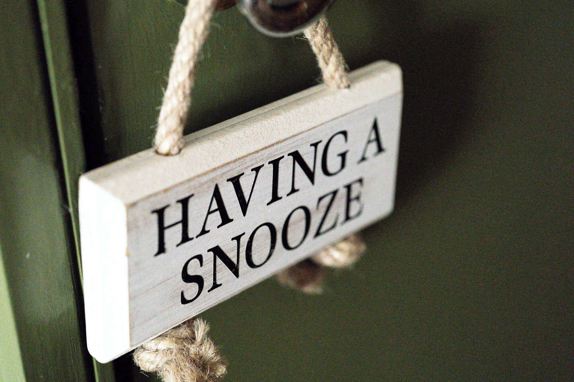 A wooden sign with the text "HAVING A SNOOZE" hanging on a door.