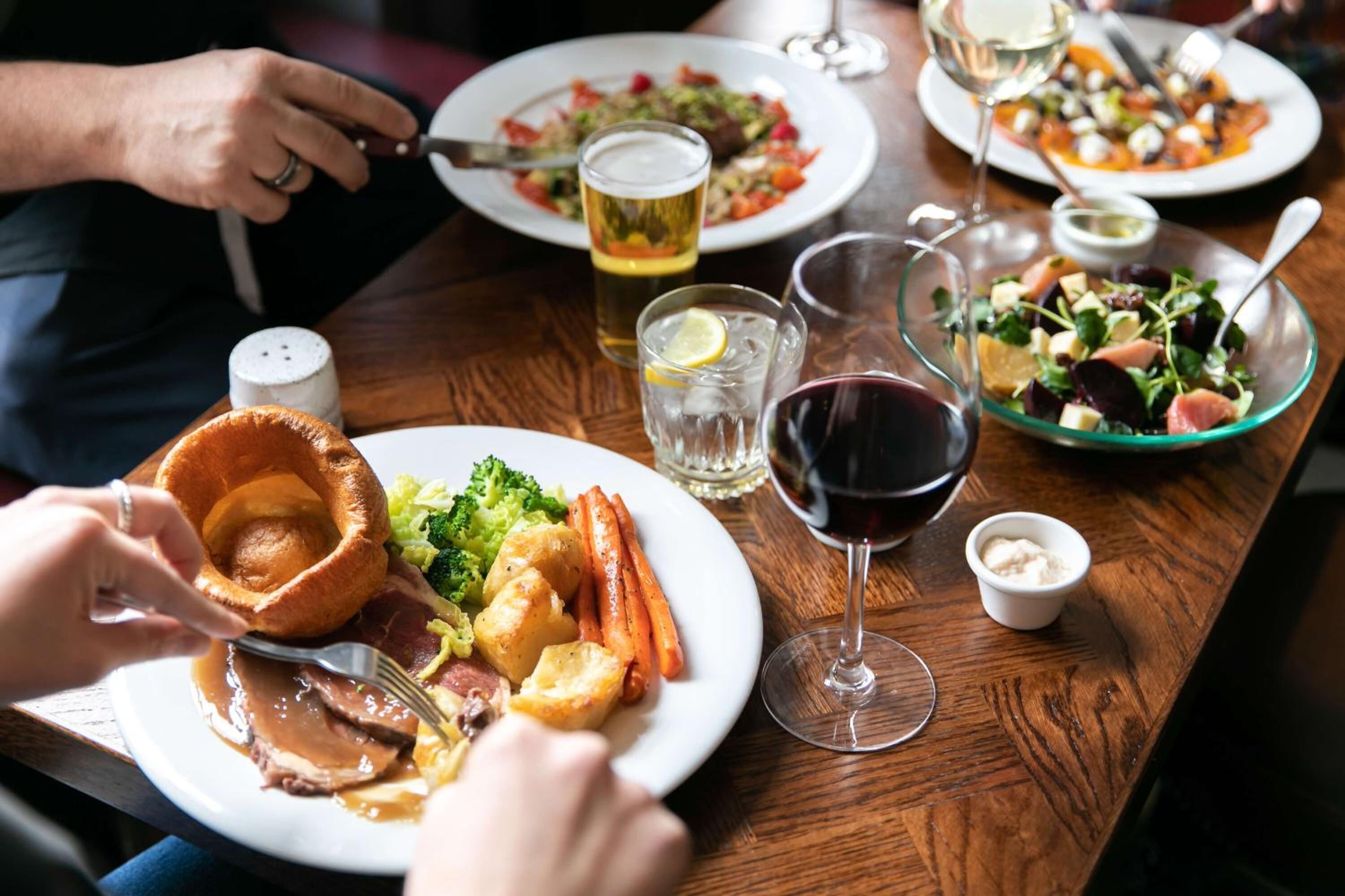 A dining table with plates of food, glasses of wine, and a salt shaker.