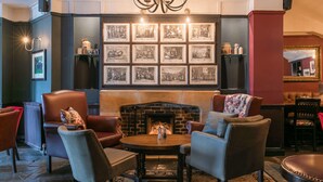 A cozy lounge area with leather armchairs, a round wooden table, and a fireplace. - The Rose & Crown Wimbledon (London)