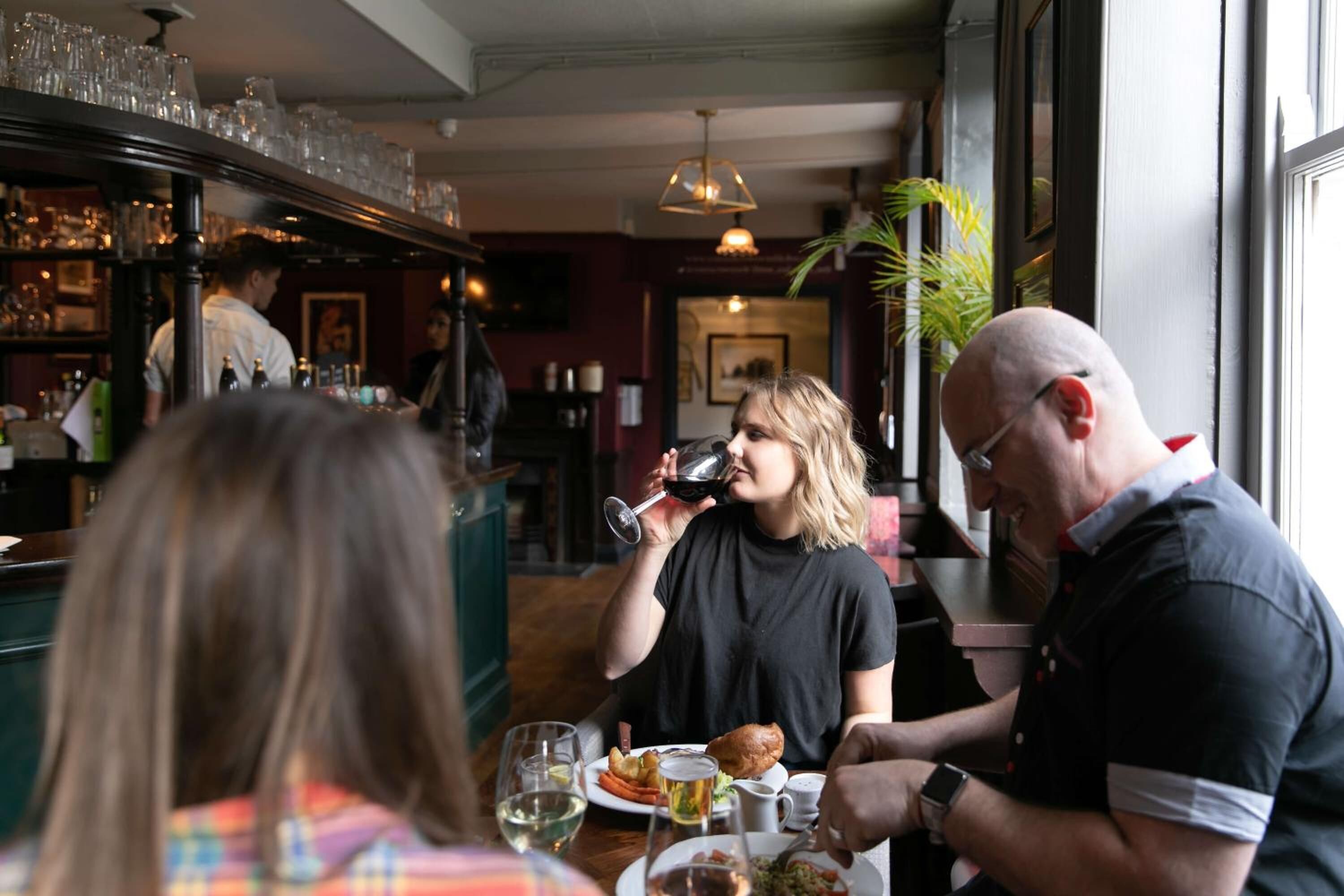 Een restaurantinterieur met een bar, eettafels en gasten.