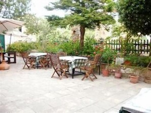 An outdoor patio with tables and chairs, surrounded by potted plants and a stone wall. - Topakas House (Chios)