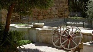 Un patio de piedra con un árbol, un muro de piedra y un par de ruedas de madera.