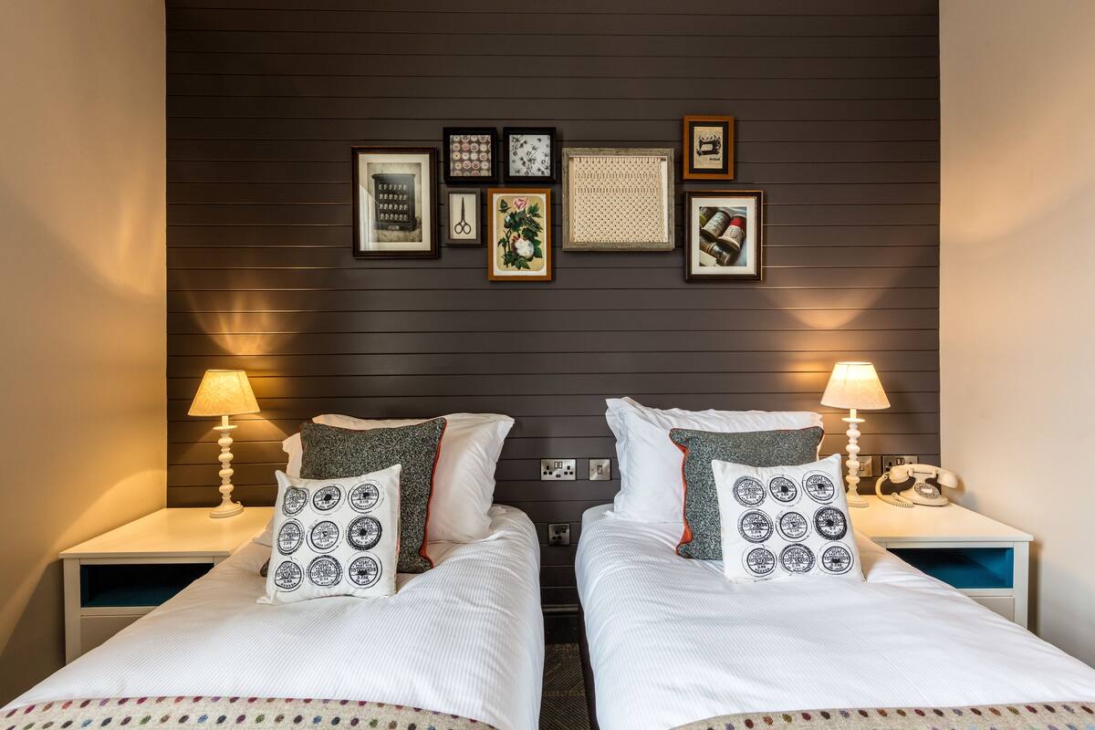 Une chambre d’hôtel avec deux lits, une tête de lit en bois foncé et un mur décoré de tableaux encadrés.