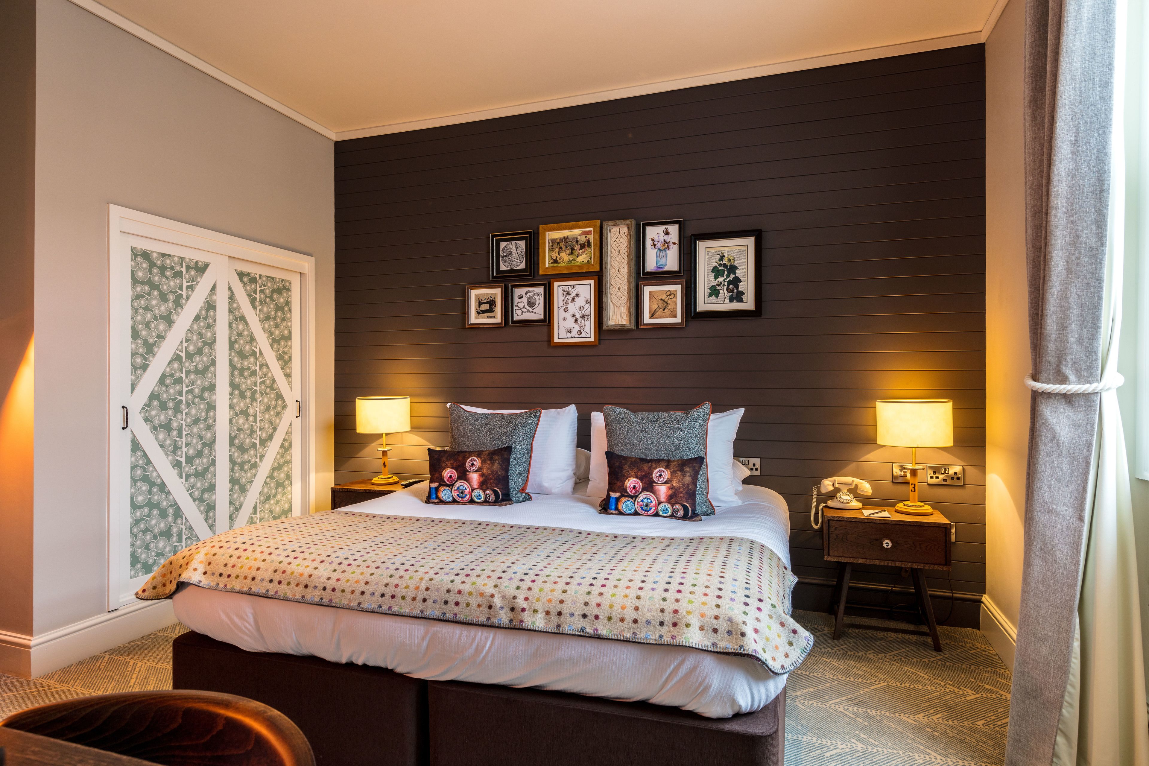 A neatly arranged bedroom with a large bed, two bedside lamps, a nightstand, and a wall adorned with framed pictures.