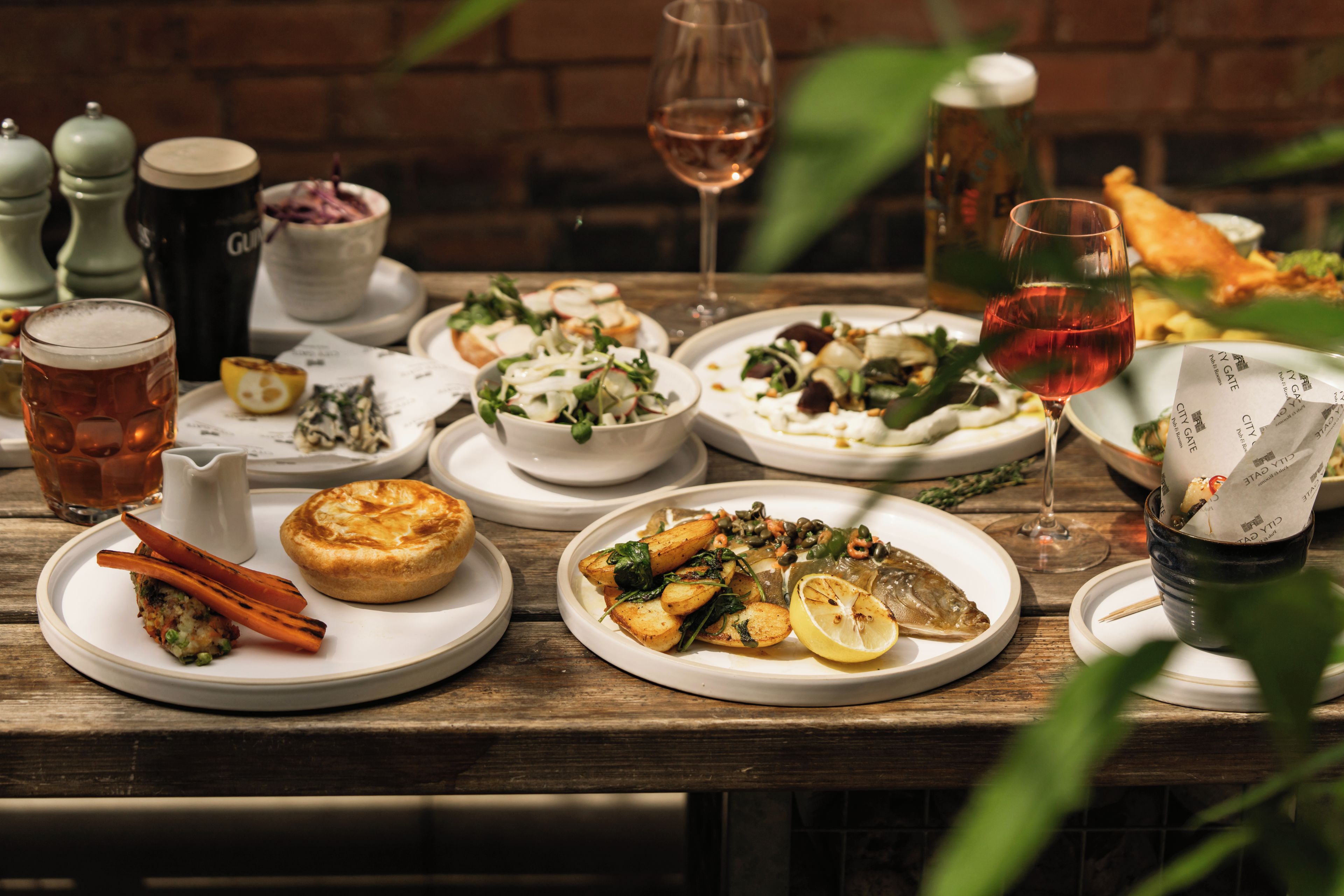 A wooden table with various dishes, glasses, and a brick wall in the background.