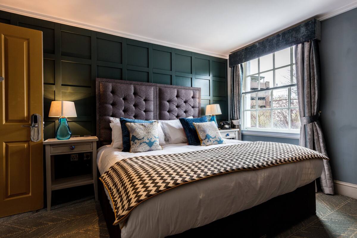 Une chambre à coucher avec un grand lit, deux tables de chevet, une commode et une fenêtre avec des rideaux.