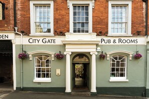 Un edificio con la señalización 'City Gate Pub & Rooms', que presenta una fachada tradicional con una entrada central, flanqueada por dos ventanas con macetas de flores.