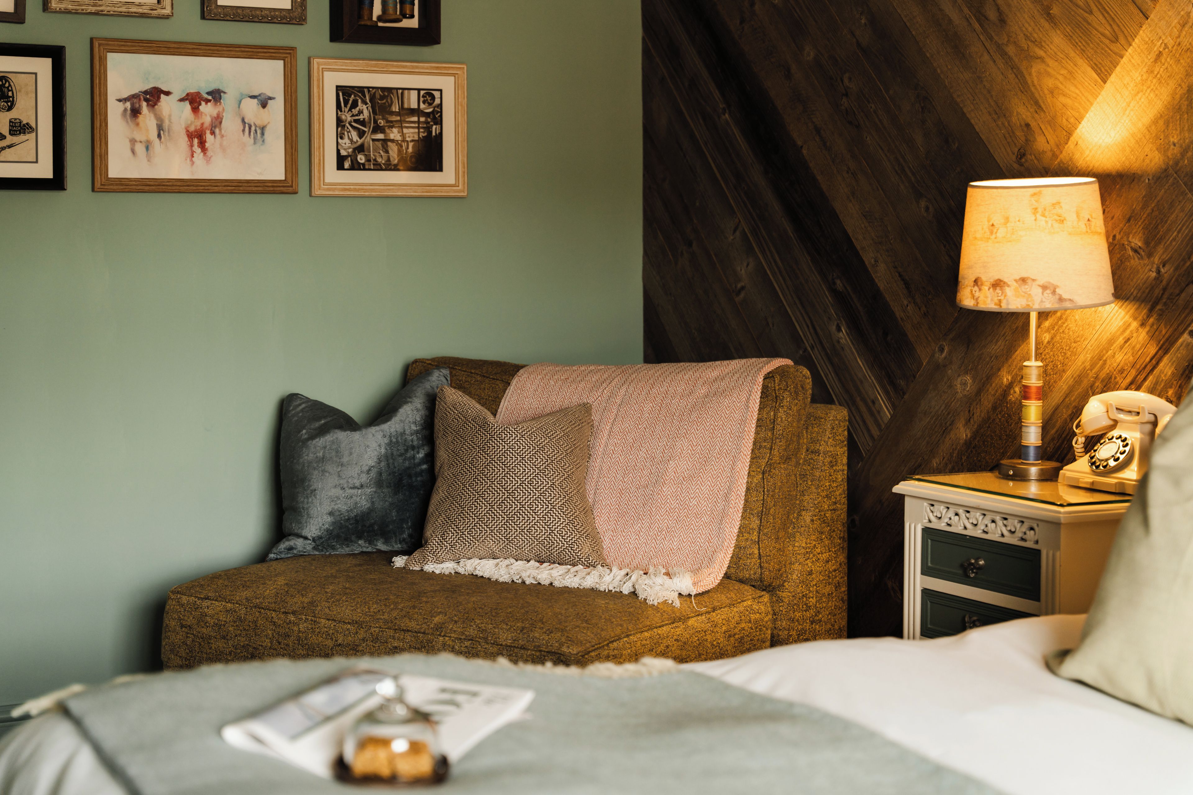A cozy room with a bed, a nightstand with a lamp, and a wall with framed pictures.
