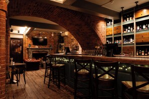 Zona de bar con paredes de ladrillo, mostrador de madera y taburetes.