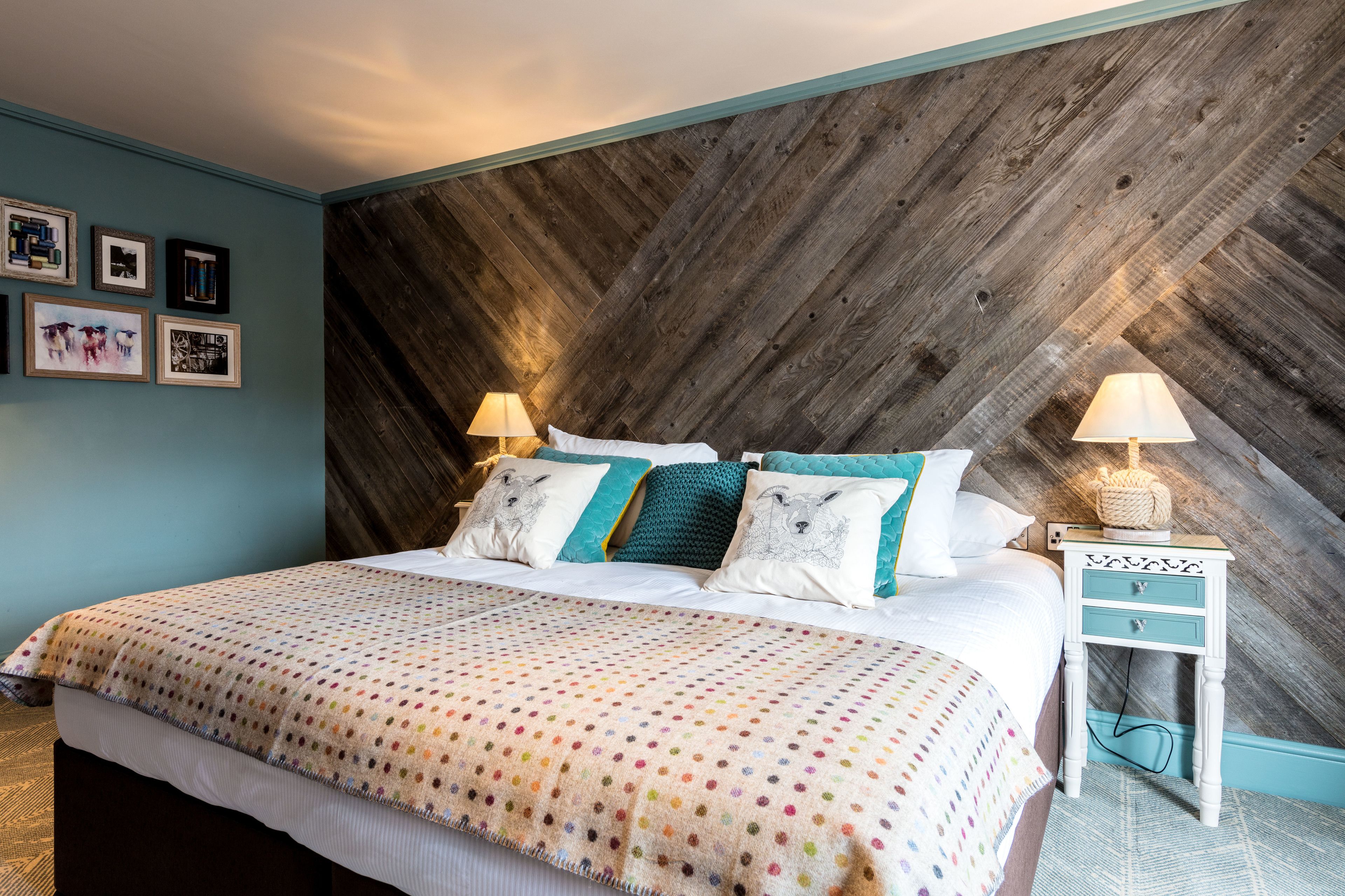 A bedroom with a bed, two bedside tables, a wall with framed pictures, and a wooden accent wall.