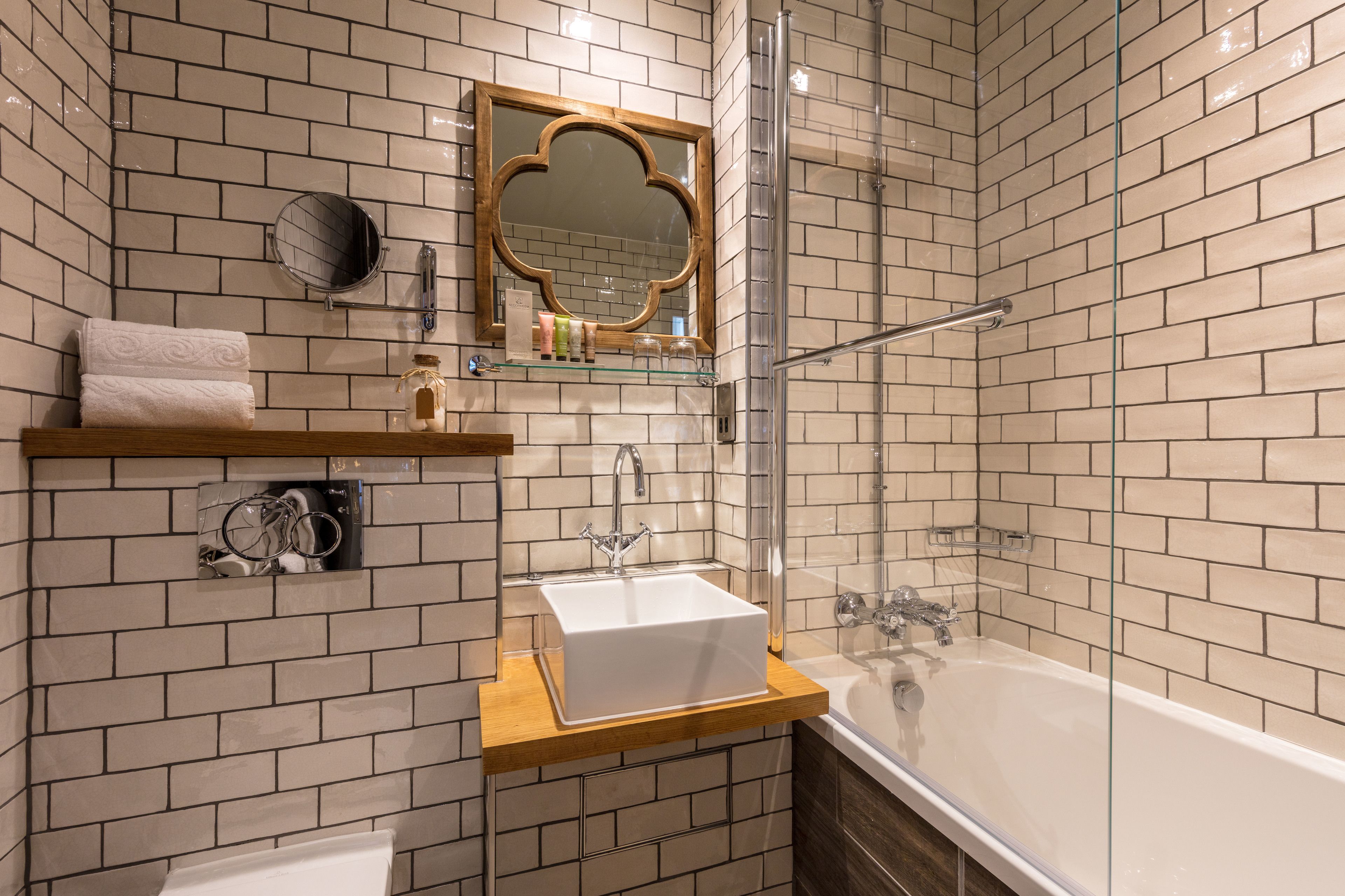 Een moderne badkamer met een witte badkuip, een douche met glazen wand en een houten wastafelmeubel met spiegel.