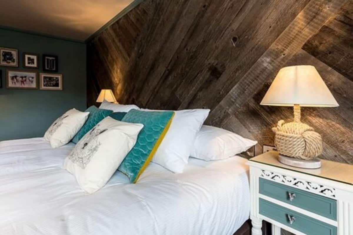 Une chambre à coucher avec un lit, des oreillers, une table de chevet avec une lampe et un mur orné de tableaux encadrés.